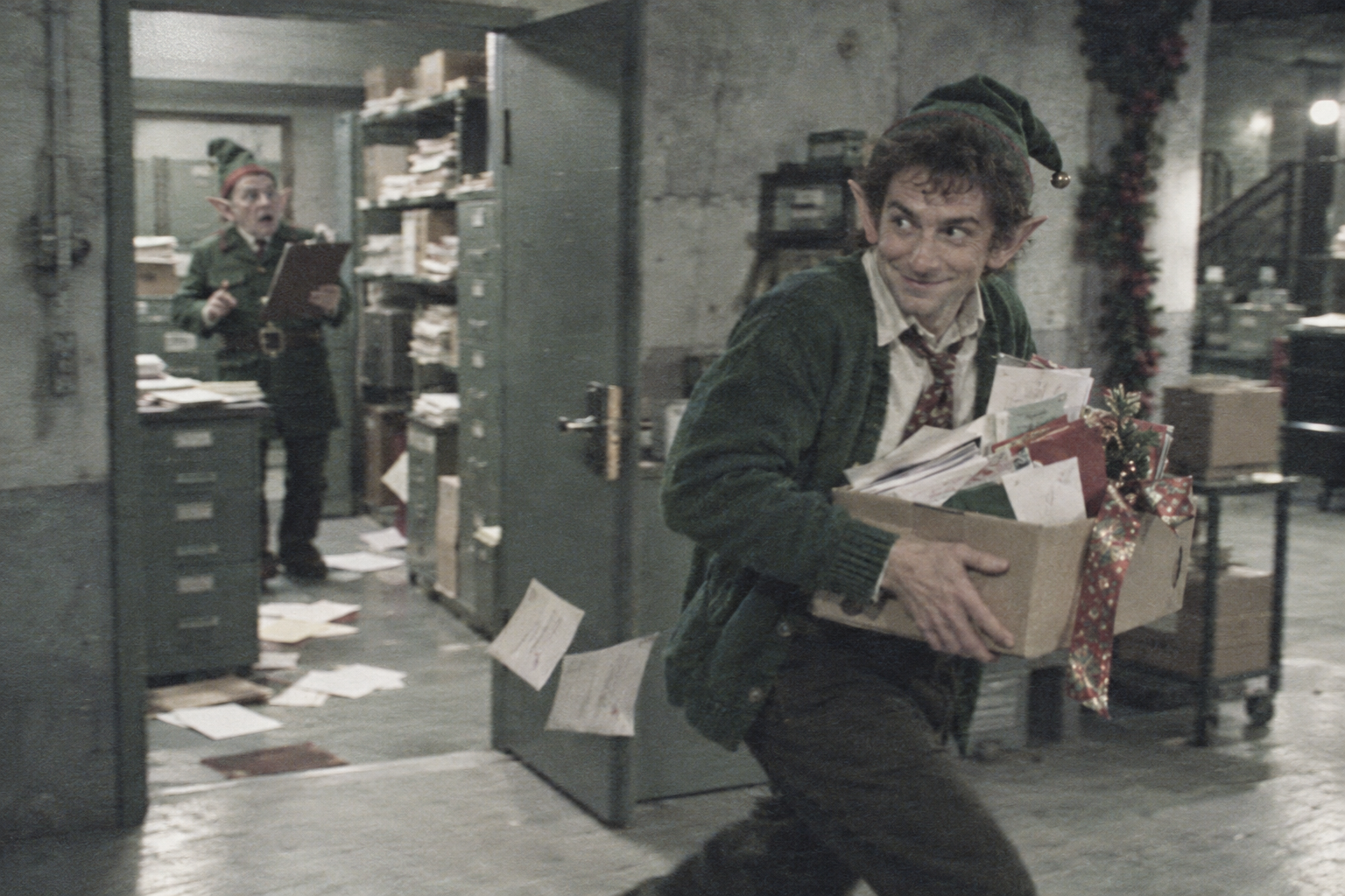 A rumpled elf carrying envelopes slips out of an administrative holding facility as a security clerk looks on.